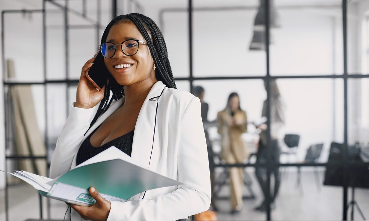A professional reviewing documents on a call, an open-plan office behind her.